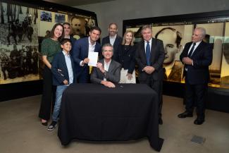 Governor Newsom hands a signed copy of Assembly Bill 2867 to author, Assemblymember Jesse Gabriel, surrounded by Mr. Gabriel's family and stakeholders